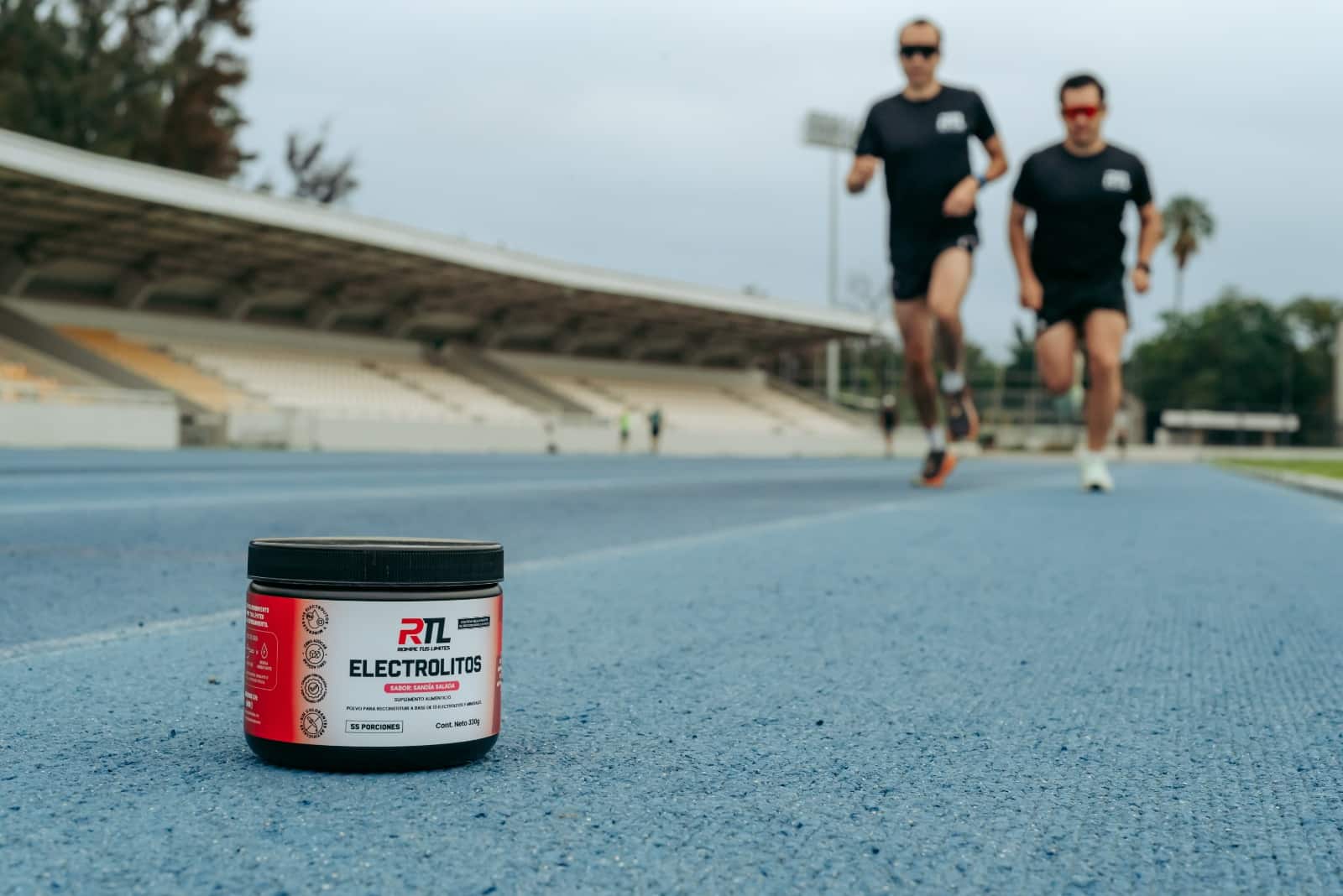 Dos corredores en pista de atletismo con el envase de Electrolitos RTL sabor Sandía Salada en primer plano