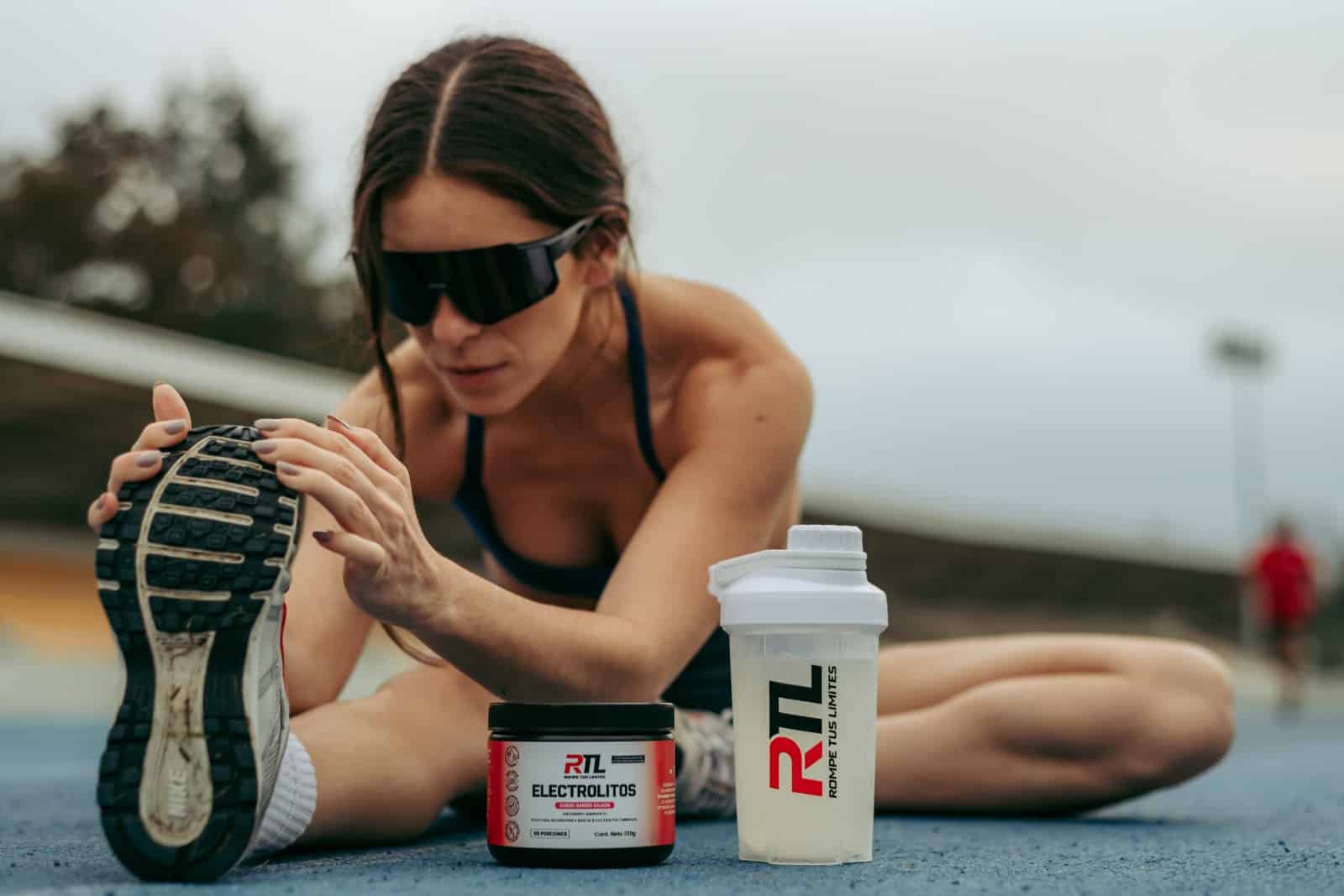 Atleta estirando en pista junto al shaker RTL y el envase de Electrolitos RTL sabor Sandía Salada